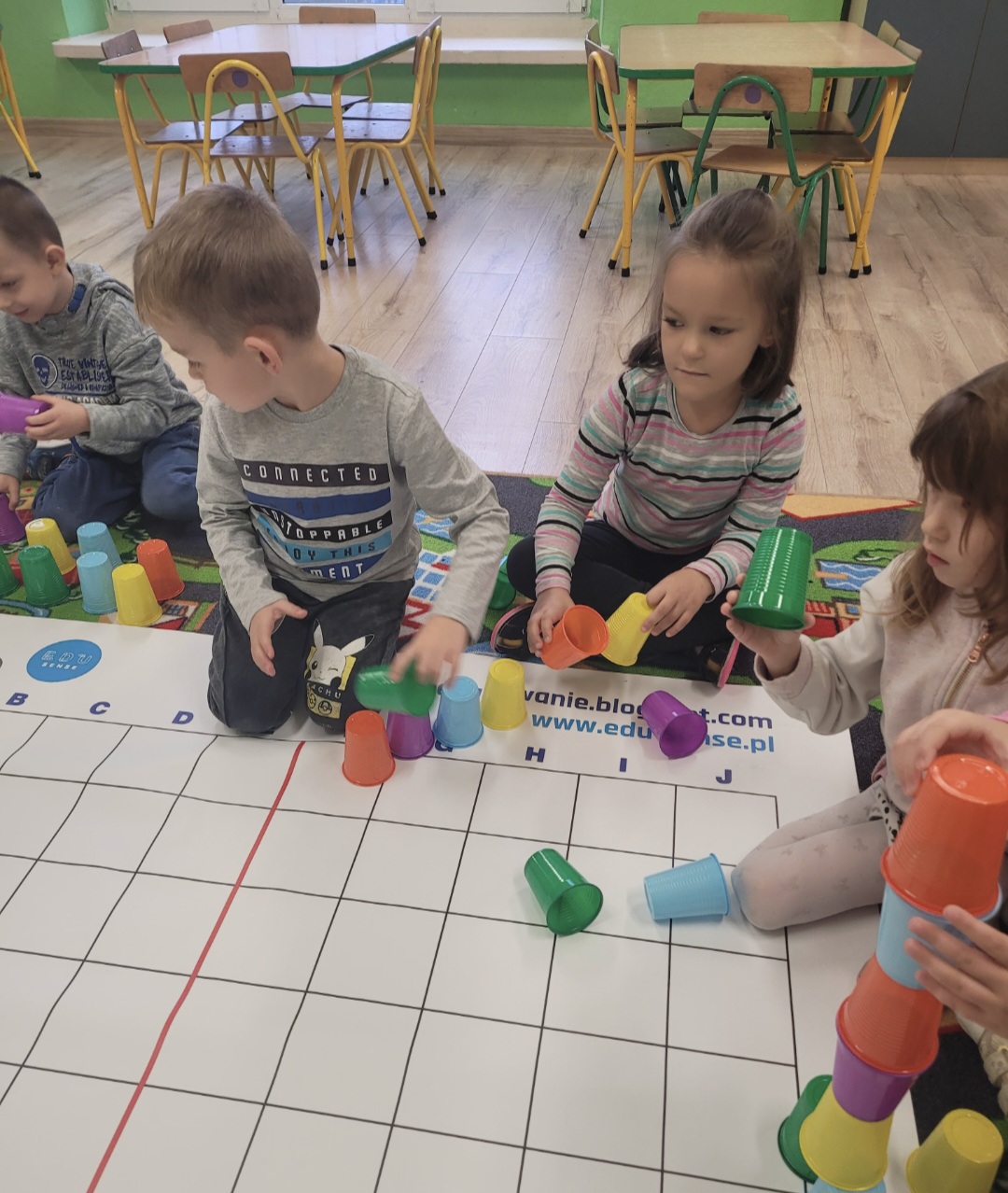 Sala przedszkolna. Dzieci budują wieżę z&nbsp;kolorowych kubk&oacute;w.