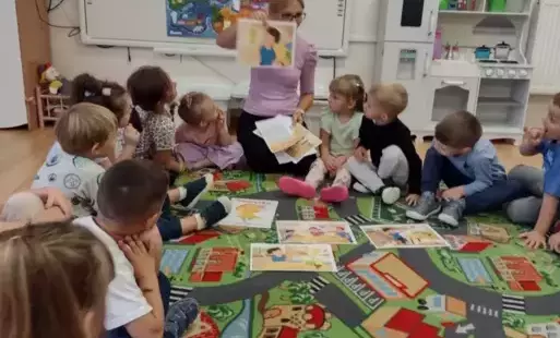 zdjęcię przedstawia sale przedszkolną. Dzieci siedzą na dywanie i przeliczają elementy.